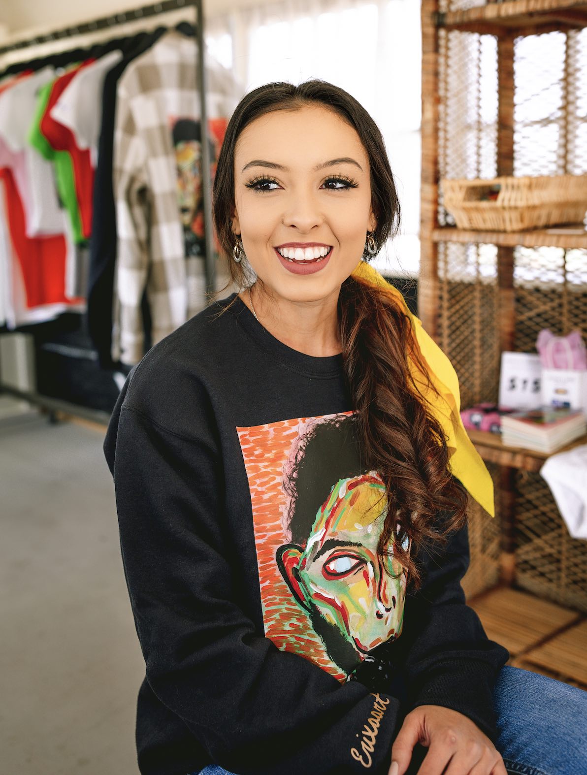 Photo of Erica Cantua (owner of Erixaart LLC) wearing black sweater with her absract art on front. Photo taken in her mobile shop which is a school bus converted into a shop. Tucson, AZ
